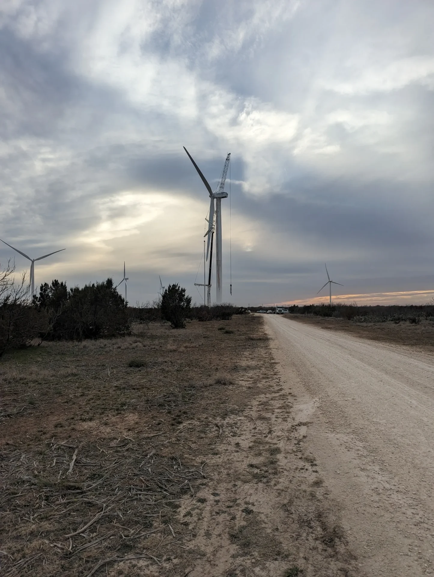 A dirt road with wind turbines in the background.